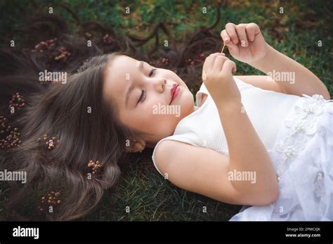 Little girl in white dress lying on the grass, she is smiling, her hair is very long and ...