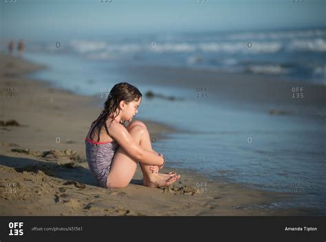 Girl sitting alone on a beach stock photo - OFFSET