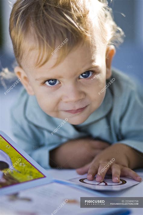 Portrait of baby boy reading picture book and looking at camera — caucasian ethnicity, indoors ...