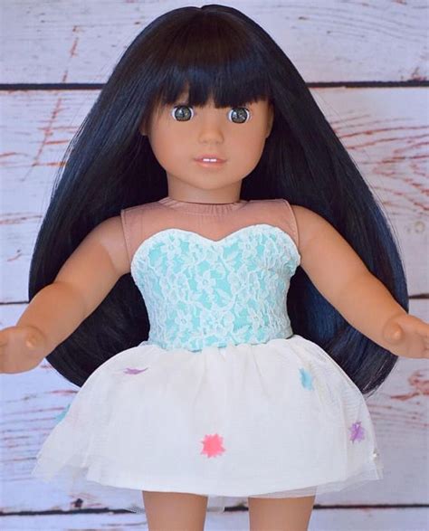 a doll with long black hair wearing a white and blue dress on a wooden surface