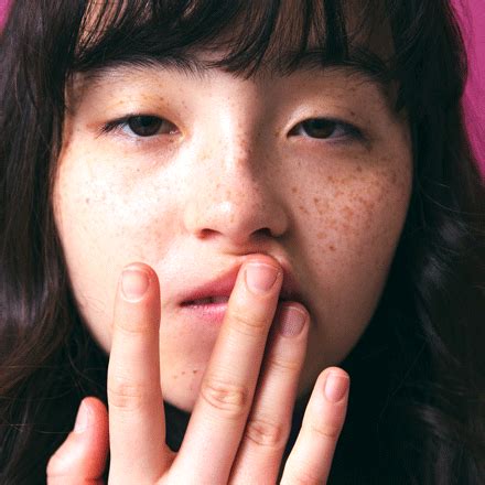 a close up of a person with freckles on her face and hand near her mouth