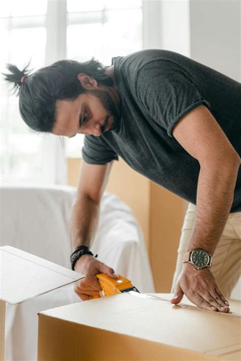 Focused young man taping cardboard box for storage · Free Stock Photo