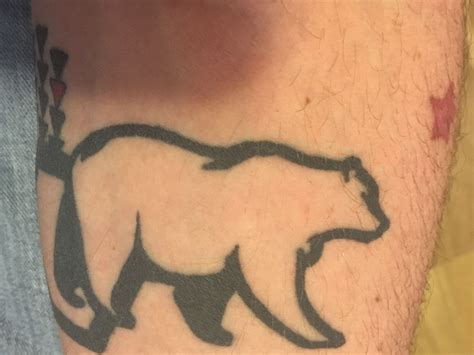 a bear tattoo on the leg of a man's left arm, with black ink