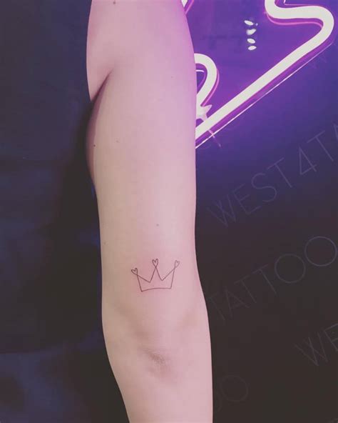 Minimalist crown tattoo on the back of the right arm.