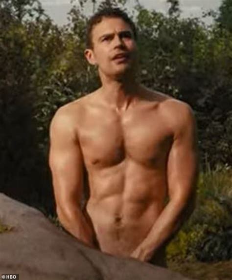 a shirtless man standing next to a rock in front of some bushes and trees