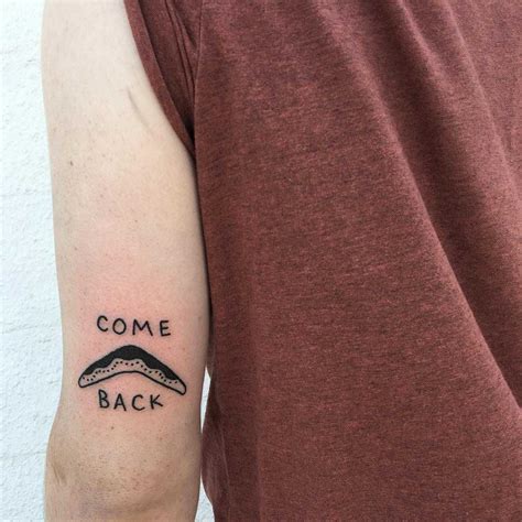 Words ‘come back’ and a tiny boomerang tattoo inked above the left elbow by tattooist yeahdope ...