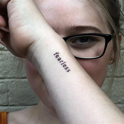 a woman wearing glasses holding her arm up to her face with the word fearless written on it