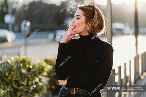 Pretty woman smoking cigarette on sunny street — fume, side view - Stock Photo | #266481810