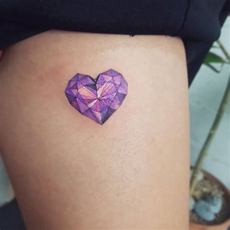 a small purple heart tattoo on the thigh