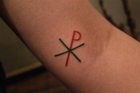 Minimalist Chi Rho symbol tattoo on the inner arm.