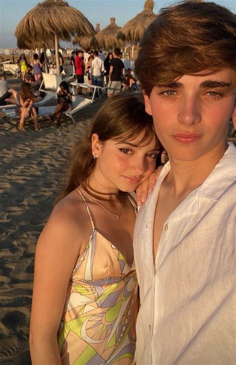 two people standing next to each other on a beach with umbrellas in the background