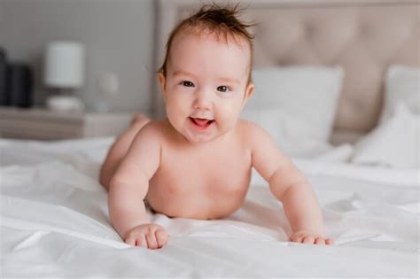 Premium Photo | Portrait of a smiling baby lying on his stomach in a bed on a white sheet