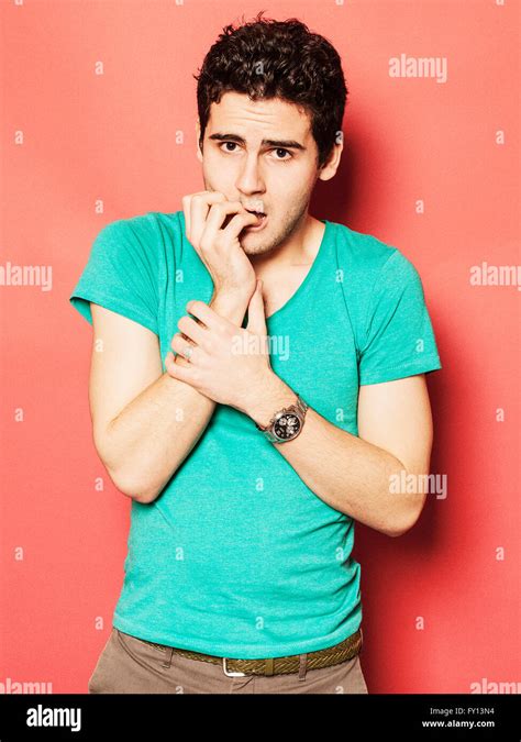 Portrait of nervous young man biting nails against red background Stock Photo - Alamy
