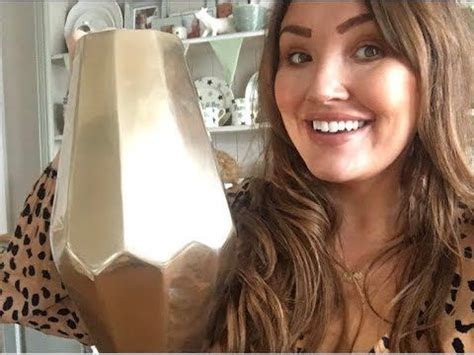 a woman holding up a gold vase in front of her face and smiling at the camera