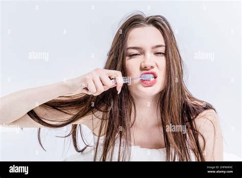 Sleepy brunette woman brushes her teeth while sitting on the bed in the ...