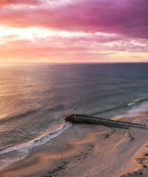 an aerial view of the beach and ocean at sunset with pink clouds in the sky