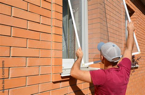 Mosquito wire screen installation. Worker installing mosquito wire screen on house window to ...