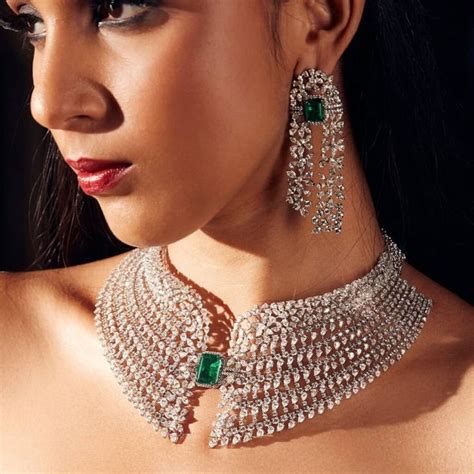 a woman wearing a necklace and earrings with emeralds on the neck, in front of a black background