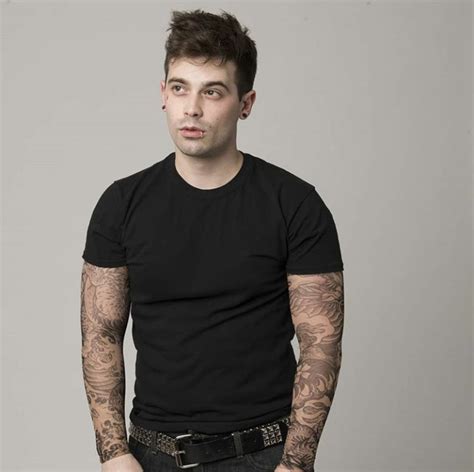 a man with tattoos standing in front of a gray background