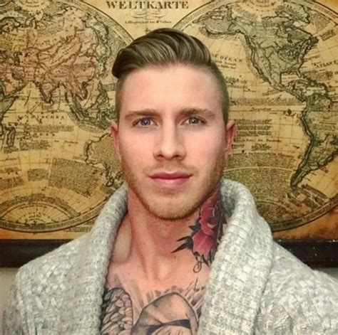 a man with tattoos standing in front of an old world map and wearing a sweater