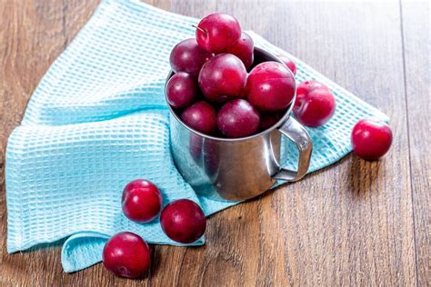 Fresh plums in an iron mug on the wooden background with a blue kitchen towel (Flip 2019 ...