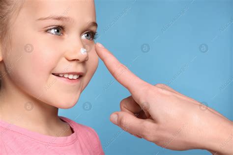 Mother applying ointment onto her daughter's nose on light blue background, closeup: Stock Photo ...