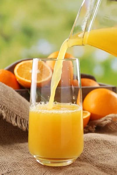 Pouring orange juice from glass carafe, on wooden table and bright ...