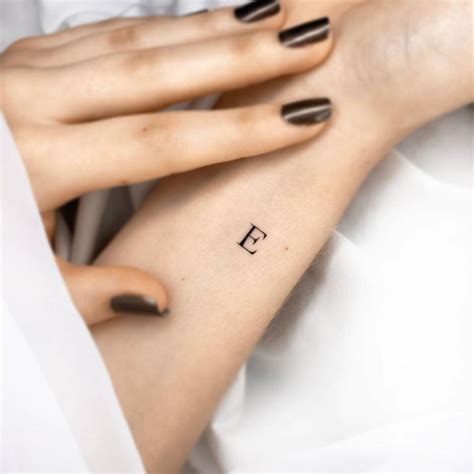 Minimalist letter "E" tattoo on the wrist.