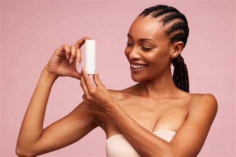 Happy african woman holding a cosmetic product. Female model with beautiful skin showing a ...