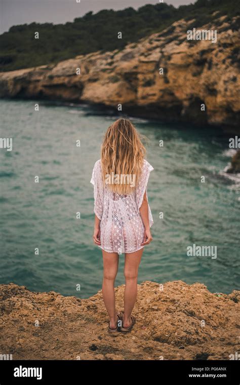 Rear view of young woman standing on a rock at the coast Stock Photo ...