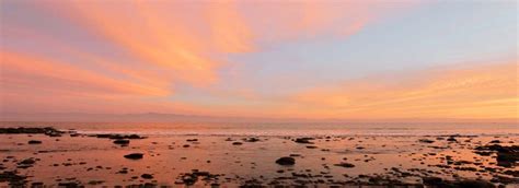 the sun is setting over the ocean and rocks