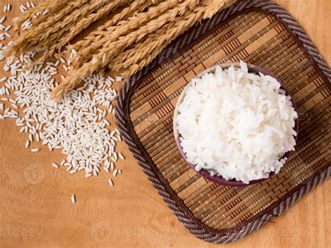 Cooked rice in bowl with raw rice grain and dry rice plant on wooden