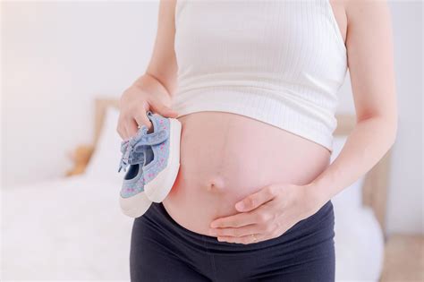 A pregnant Asian woman stands in her bedroom and prepares a small pair