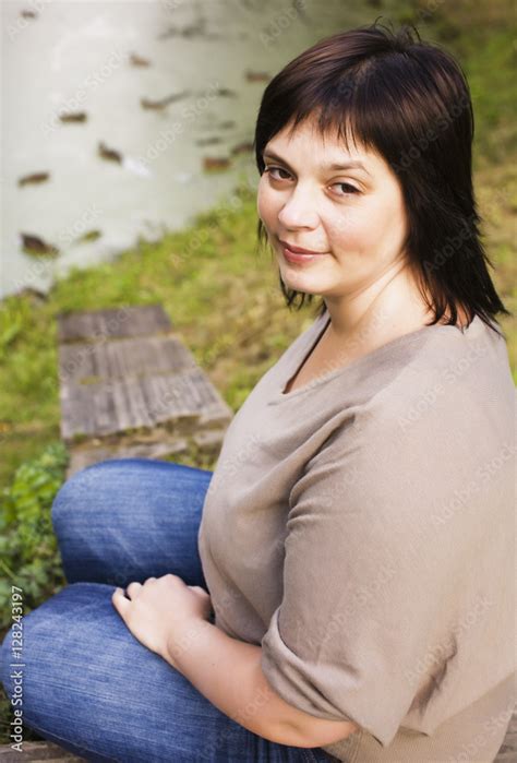 mature brunette fat woman in green garden, smiling, friendly welkoming