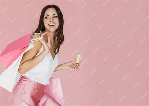 Mujer con bolsas de compras y una rosquilla sobre fondo rosa | Foto Gratis