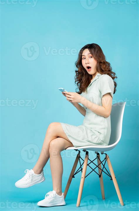 Young Asian girl sitting in chair using phone with surprised expression