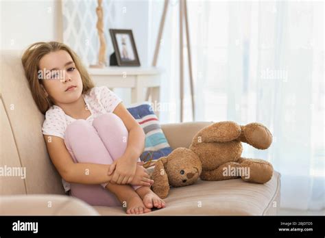 Sad little girl sitting on couch in room Stock Photo - Alamy
