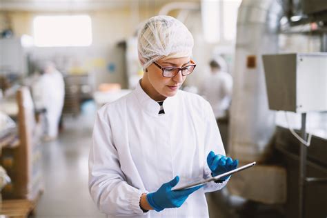 Young focused female worker in sterile clothes checking productivity of