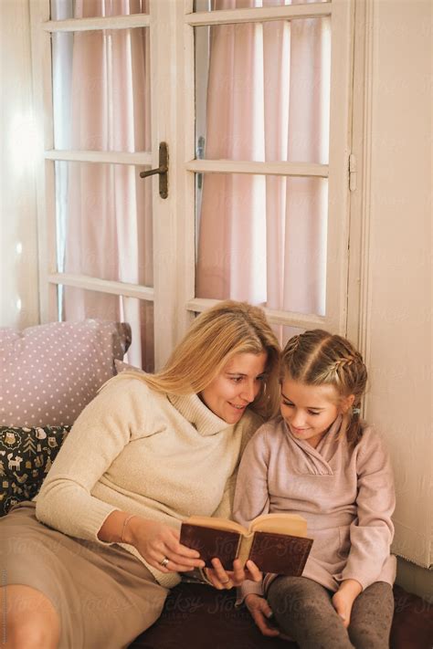 "Mother And Daughter Sitting On Bed And Reading A Book" by Stocksy