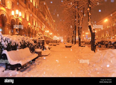 Snowfall in city center at night. Snow illuminated by street lanterns. Everything covered by ...