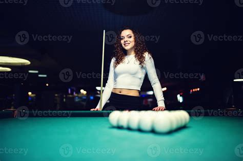 Young curly girl posed near billiard table. Sexy model at black mini