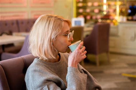 Premium Photo | Young attractive blonde girl in cafe drinks coffee from ...