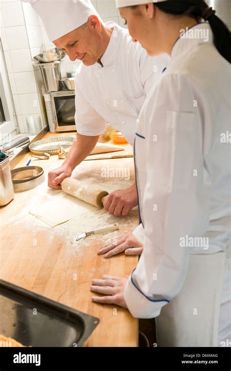 Male chef rolling dough with rolling pin assistant watching Stock Photo ...