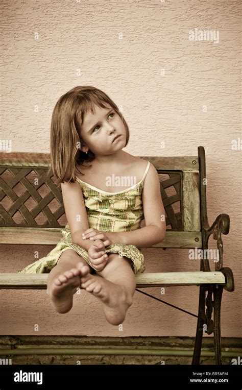 Portrait of cute child sitting on bench and stretching barefoot legs ...