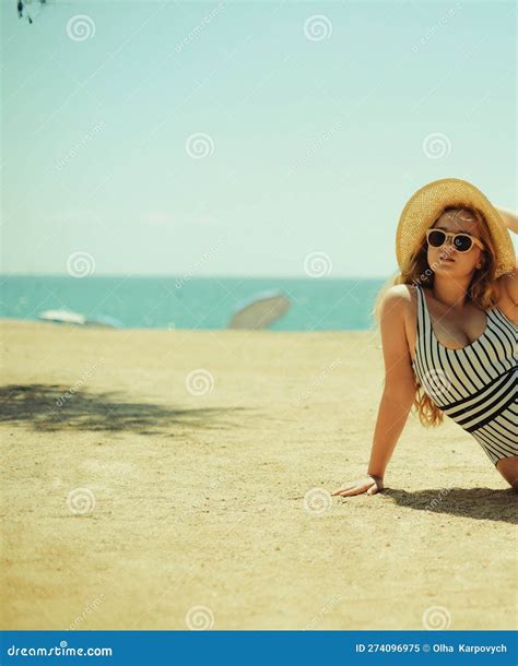 A Beautiful Blonde is Sunbathing on the Beach in a One-piece Swimsuit