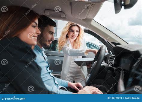 Young Couple in Car. Female Dealership Consultant Shows a Car To a ...