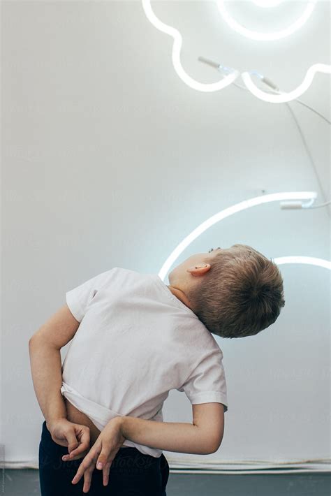"A Boy Twists His Hands Behind His Back As He Looks Up At LED Tubes On