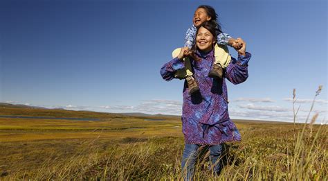 Alaska Native Athabascan girls in traditional kuspuks doing piggy-back ride in tundra outside