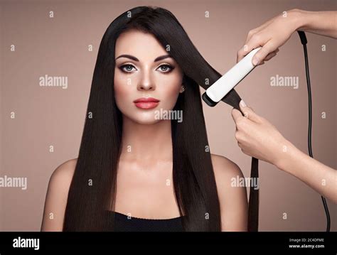 Hairdresser straightening long dark hair with hair irons. Beautiful ...