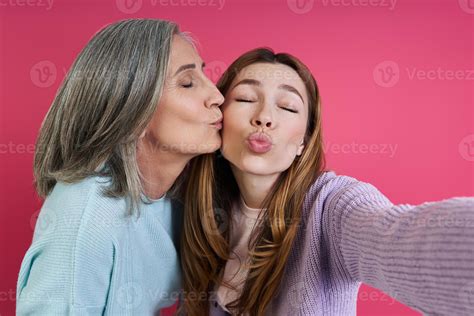 Senior mother kissing her adult daughter while making selfie against
